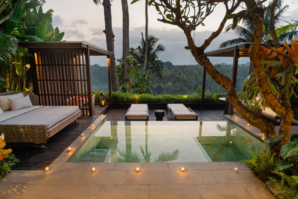 Romantic honeymoon villa in Bali with a private pool, lounge chairs and a cozy gazebo overlooking lush jungle at dusk, with candles lining the poolside