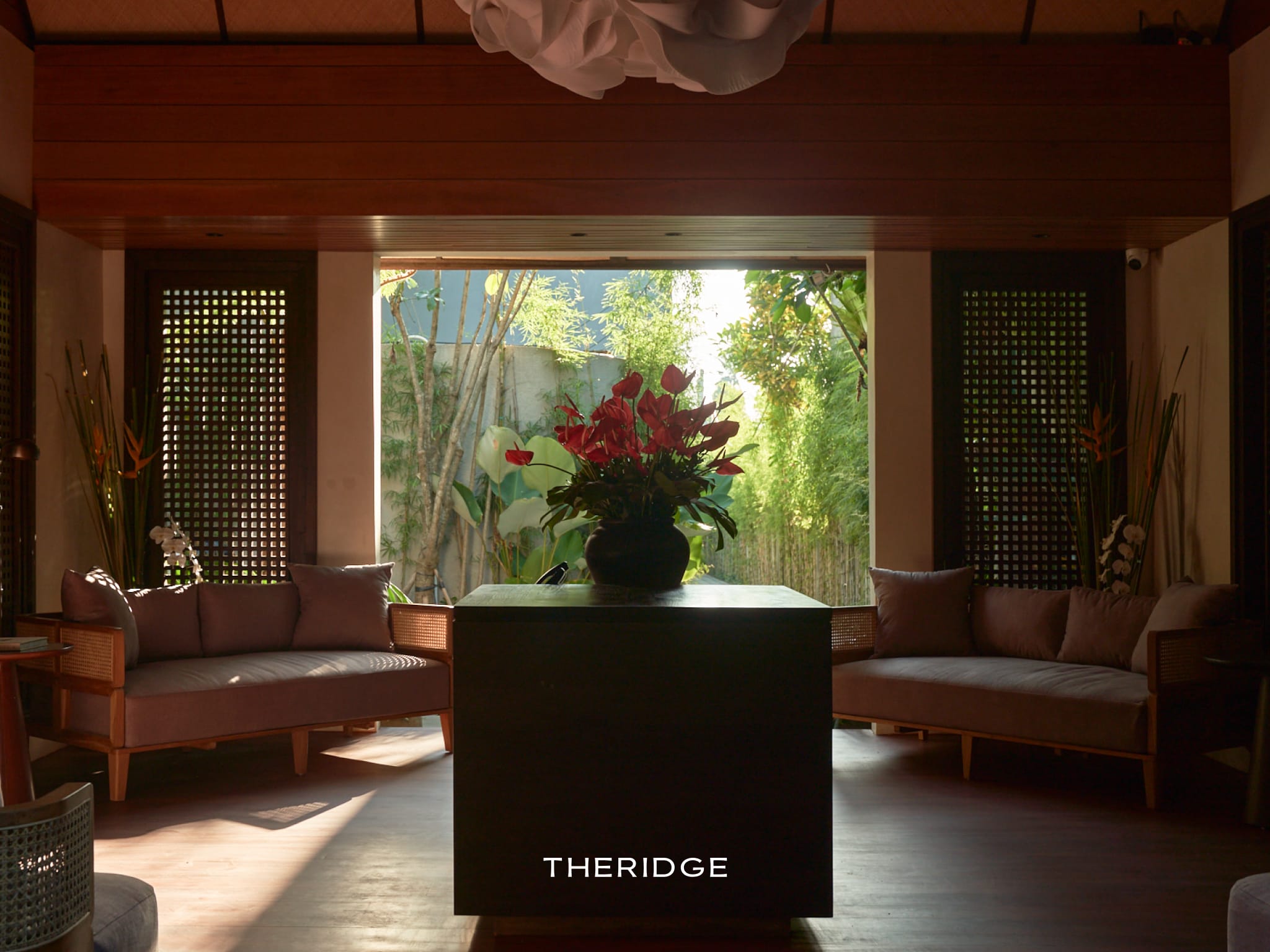 The serene and elegant interior of a luxury villa lounge near Ubud Market, featuring traditional wooden furniture, warm sunlight, and a large red floral centerpiece.